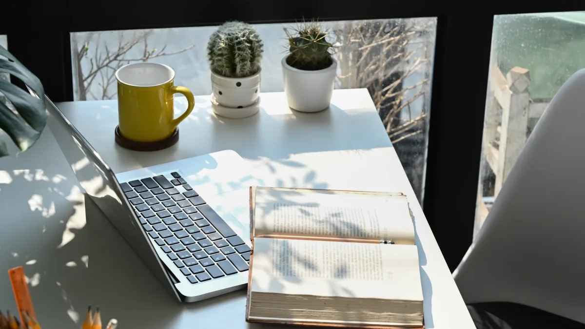 Open book and laptop on a writing desk by a window