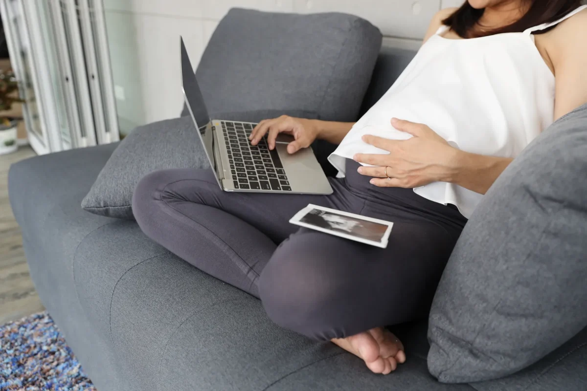Pregnant woman reading on a laptop at home with an ultrasound photo